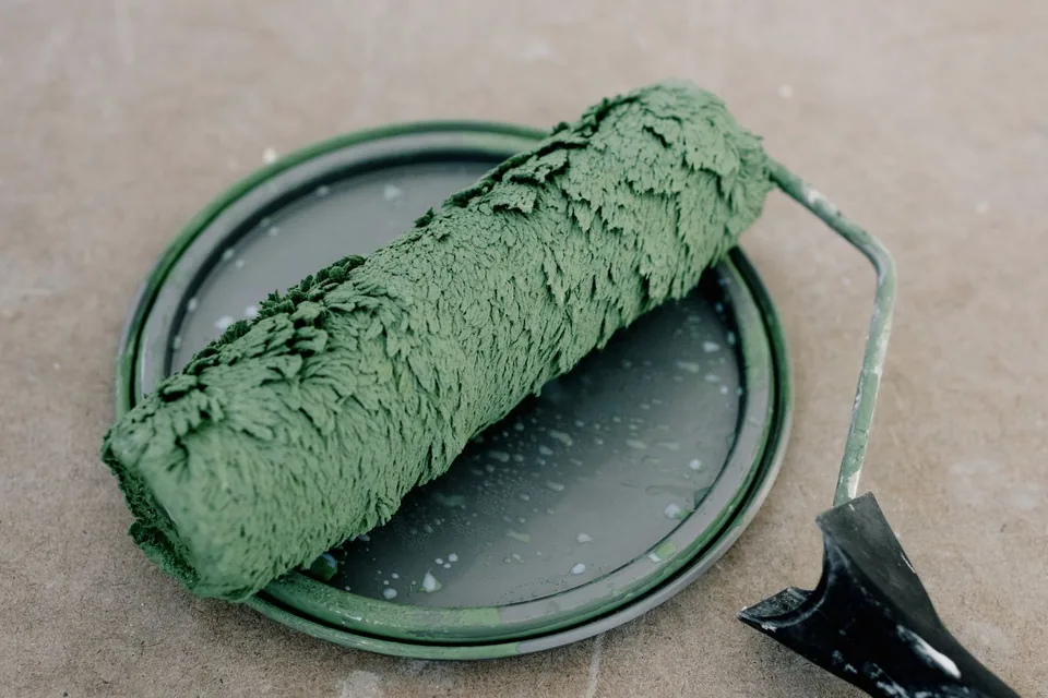 Verfroller met groene verf op het deksel van een verfblik